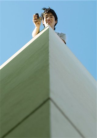 simsearch:695-03373539,k - Young man using cell phone on top of building, low angle view Stock Photo - Premium Royalty-Free, Code: 695-03373542