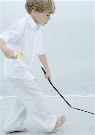 stepping on flowers - Little boy walking alongside surf on beach, holding flowers in one hand and stick in the other Stock Photo - Premium Royalty-Free, Code: 695-03373632