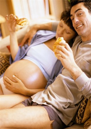 pregnancy and eating - Man and pregnant woman eating croissants on sofa Stock Photo - Premium Royalty-Free, Code: 695-03384016