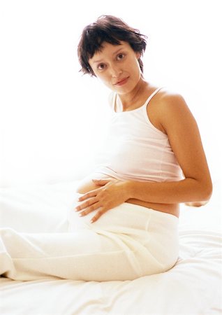 simsearch:633-05401926,k - Femme enceinte assis avec la main sur le ventre, en regardant la caméra, portrait Photographie de stock - Premium Libres de Droits, Code: 695-03384056