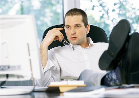 surprised adult work casual - Businessman holding glasses next to face, looking at computer screen, sitting with feet on desk Stock Photo - Premium Royalty-Free, Code: 695-03384091