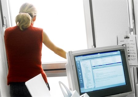 simsearch:859-06537734,k - Woman in office standing and looking out of window, computer monitor in foreground Fotografie stock - Premium Royalty-Free, Codice: 695-03384162