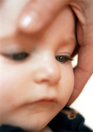 Adult hand around baby's face, close-up Stock Photo - Premium Royalty-Free, Code: 695-03384976