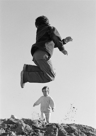 Boy jumping and little girl walking in background, low angle view, b&w Stock Photo - Premium Royalty-Free, Code: 695-03385080