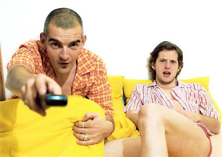 Two men sitting on sofa, one pointing remote control at camera Foto de stock - Sin royalties Premium, Código: 695-03385900