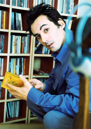 Young man in front of cd collection, looking into camera, portrait. Stock Photo - Premium Royalty-Free, Code: 695-03385912