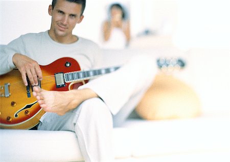 Man playing guitar, woman blurred in background Stock Photo - Premium Royalty-Free, Code: 695-03387132