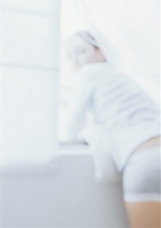 simsearch:633-01992734,k - Woman leaning on windowsill looking over shoulder at camera, blurred Foto de stock - Royalty Free Premium, Número: 695-03387571