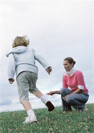 Woman crouching holding end of jump rope for boy preparing to jump Stock Photo - Premium Royalty-Free, Code: 695-03388093