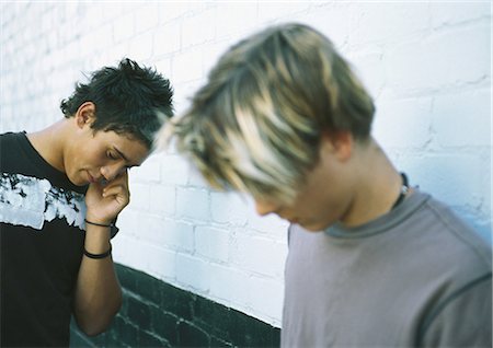 Two teenage boys standing next to brick wall, one using cell phone Stock Photo - Premium Royalty-Free, Code: 695-03388142
