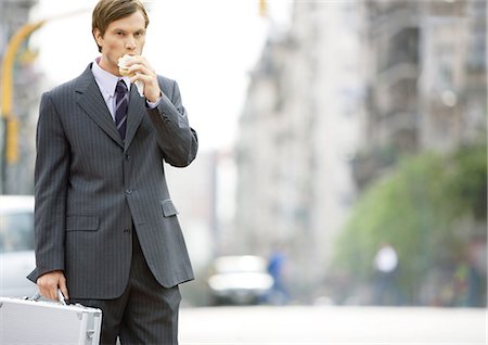 street businessman walking - Businessman in the street, eating on the go Stock Photo - Premium Royalty-Free, Code: 695-03388358