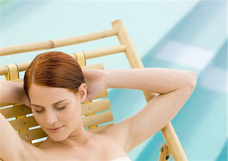 portrait and woman and closeup and arms - Woman sitting in deckchair with hands behind head and eyes closed, pool in background Stock Photo - Premium Royalty-Free, Code: 695-03388417