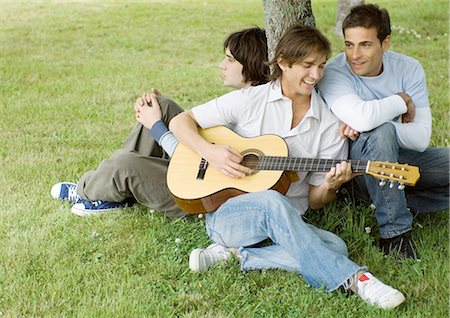 simsearch:695-05778554,k - Young male friends sitting near tree, playing guitar Fotografie stock - Premium Royalty-Free, Codice: 695-03388544