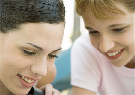 simsearch:695-03388448,k - Young woman and girl looking down and smiling, portrait, extreme close-up Fotografie stock - Premium Royalty-Free, Codice: 695-03388633