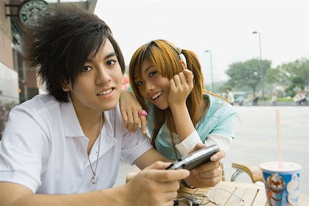 simsearch:855-02989409,k - Teenage couple sitting at outdoor cafe, boy holding video game Stock Photo - Premium Royalty-Free, Code: 695-03388892