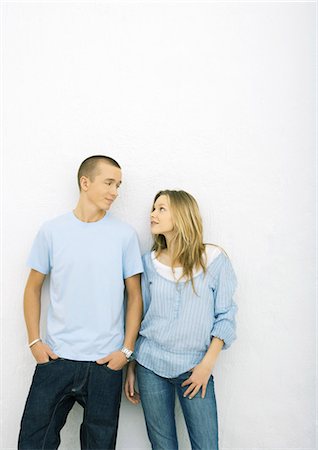 Young couple standing side by side, leaning against wall, looking at each other, three quarter length Foto de stock - Sin royalties Premium, Código: 695-03388937