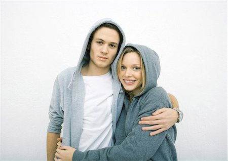 Young couple standing with arms around each other, wearing hooded sweatshirts, looking at camera Stock Photo - Premium Royalty-Free, Code: 695-03388932