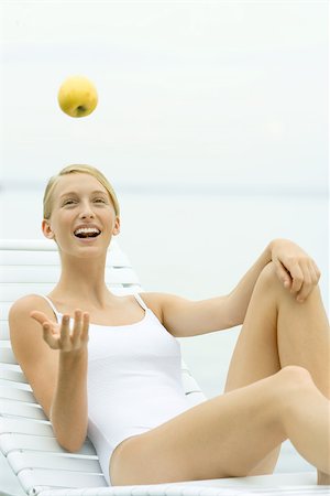 simsearch:695-03378760,k - Teenage girl in swimsuit sitting on lounge chair, catching apple Foto de stock - Sin royalties Premium, Código: 695-03389067