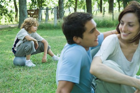 Family sitting on grass outdoors, focus on boy sitting on ball in background Stock Photo - Premium Royalty-Free, Code: 695-03389194