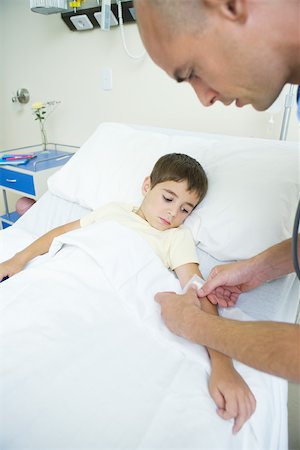 person in hospital bed overhead - Boy lying in hospital bed while doctor puts bandage on boy's arm Stock Photo - Premium Royalty-Free, Code: 695-03389200