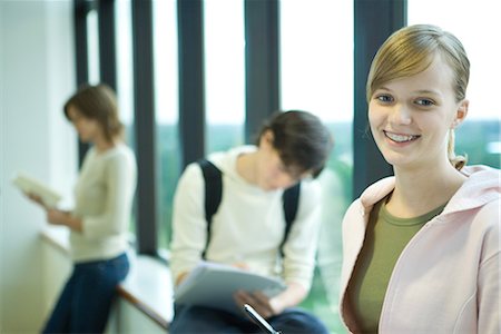 simsearch:632-01380712,k - Female student in front of window, smiling at camera, peers in background Fotografie stock - Premium Royalty-Free, Codice: 695-03389409