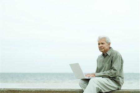 Senior man sitting near water's edge, using laptop Stock Photo - Premium Royalty-Free, Code: 695-03389521