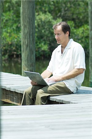 Man sitting on dock, using laptop computer, looking away Stock Photo - Premium Royalty-Free, Code: 695-03389522