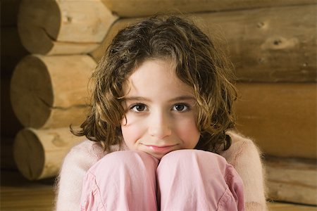 Girl sitting with head resting on knees, smiling at camera Stock Photo - Premium Royalty-Free, Code: 695-03389565