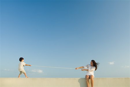 Boy and woman playing tug of war, blue sky in background Stock Photo - Premium Royalty-Free, Code: 695-03389665