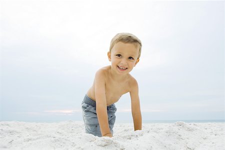 Little boy crouching at the beach, smiling at camera, portrait Stock Photo - Premium Royalty-Free, Code: 695-03389777