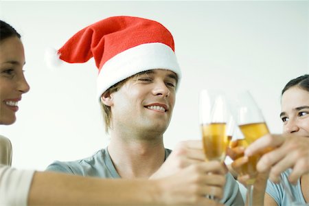 simsearch:614-06311930,k - Adult friends clinking champagne glasses, smiling, focus on man in Santa hat, cropped Stock Photo - Premium Royalty-Free, Code: 695-03389850