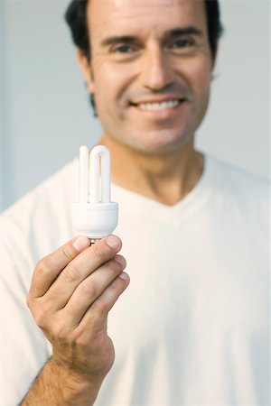 Man holding energy efficient light bulb, smiling at camera Stock Photo - Premium Royalty-Free, Code: 695-03389878