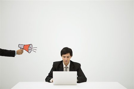 Hand aiming megaphone at young professional using laptop Stock Photo - Premium Royalty-Free, Code: 695-03389943