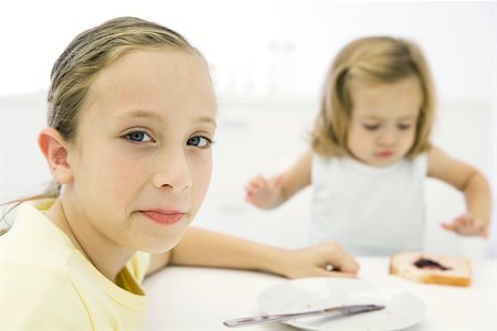 simsearch:695-03380035,k - Girl sitting at table with younger sister, smiling over shoulder at camera Foto de stock - Royalty Free Premium, Número: 695-03380035