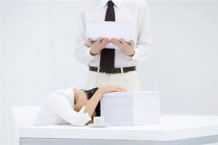 simsearch:695-05768442,k - Woman with head down on desk, next to tall stack of papers, man holding another stack of paper Stock Photo - Premium Royalty-Free, Code: 695-03380039