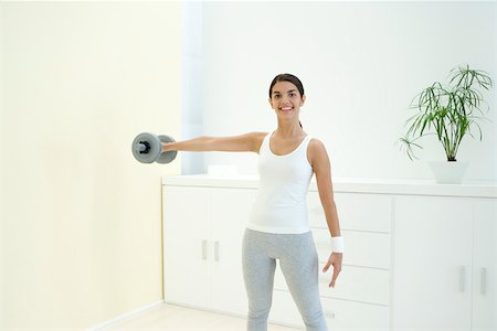 simsearch:693-06323954,k - Young woman lifting weights at home, smiling at camera Fotografie stock - Premium Royalty-Free, Codice: 695-03380076