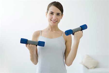 simsearch:693-06323954,k - Young woman lifting dumbbells, smiling at camera Fotografie stock - Premium Royalty-Free, Codice: 695-03380082
