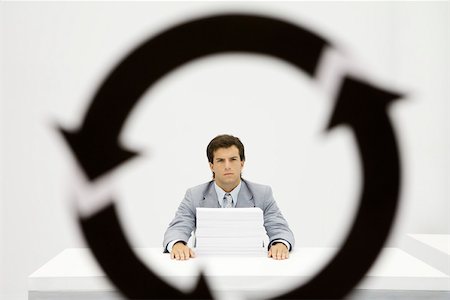 Professional sitting at desk with large stack of paper, circular arrow symbol in foreground Stock Photo - Premium Royalty-Free, Code: 695-03380193