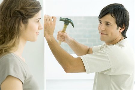 Couple smiling at each other, man hammering nail into wall Foto de stock - Sin royalties Premium, Código: 695-03380210