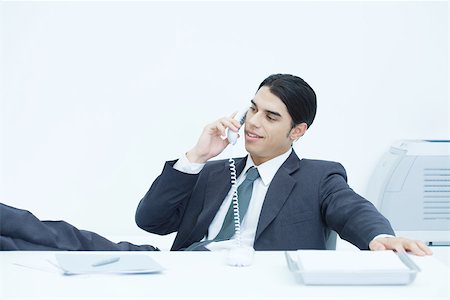 Young businessman sitting with feet up at desk, talking on landline phone Stock Photo - Premium Royalty-Free, Code: 695-03380256