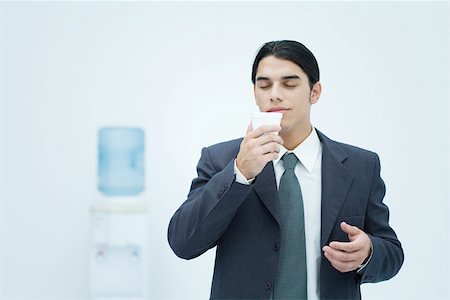 plastic cup people not birthday not wedding - Businessman holding and smelling disposable cup with eyes closed, water cooler in background Stock Photo - Premium Royalty-Free, Code: 695-03380259