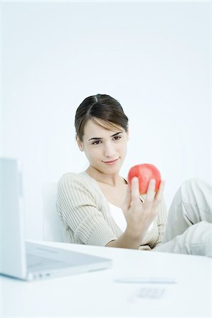 photo of desk with apple laptop - Young woman holding apple, looking down Stock Photo - Premium Royalty-Free, Code: 695-03380261