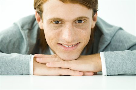 simsearch:695-03380090,k - Young man resting head on folded arms, smiling at camera, portrait Stock Photo - Premium Royalty-Free, Code: 695-03380300