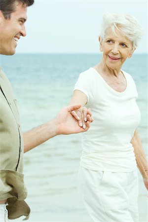 senior woman and son affection - Senior woman walking hand in hand with adult son by water, smiling at each other Stock Photo - Premium Royalty-Free, Code: 695-03380398