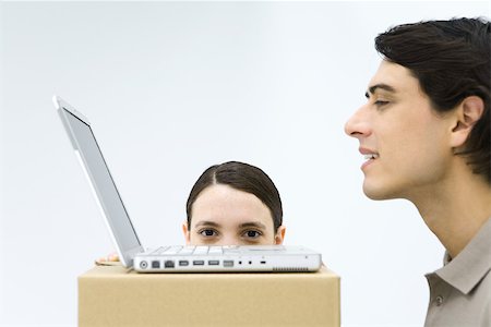 simsearch:693-06121395,k - Man using laptop computer at cardboard box desk, woman hiding behind box, peeking over edge Foto de stock - Royalty Free Premium, Número: 695-03380456