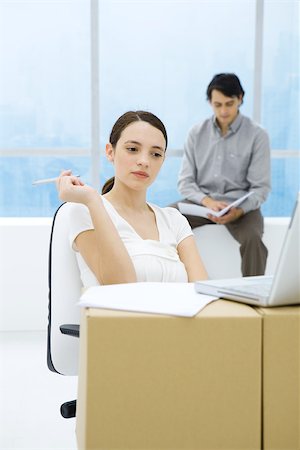Young woman sitting at cardboard box desk, looking at laptop computer Stock Photo - Premium Royalty-Free, Code: 695-03380453