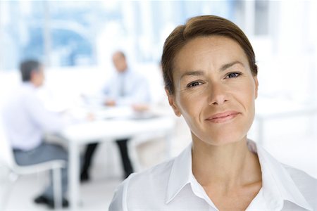 Professional woman smiling at camera, portrait, male colleagues working in background Foto de stock - Sin royalties Premium, Código: 695-03380520