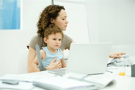 desk toy - Woman sitting at desk with toddler on her lap, hanging up landline phone Stock Photo - Premium Royalty-Free, Code: 695-03380539