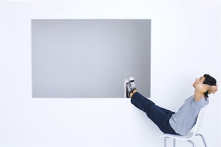 Man sitting in chair with hands behind head and legs up, looking up Stock Photo - Premium Royalty-Free, Code: 695-03380568