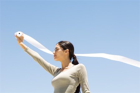 Woman holding up roll of paper outdoors, eyes closed, low angle view Stock Photo - Premium Royalty-Free, Code: 695-03380592